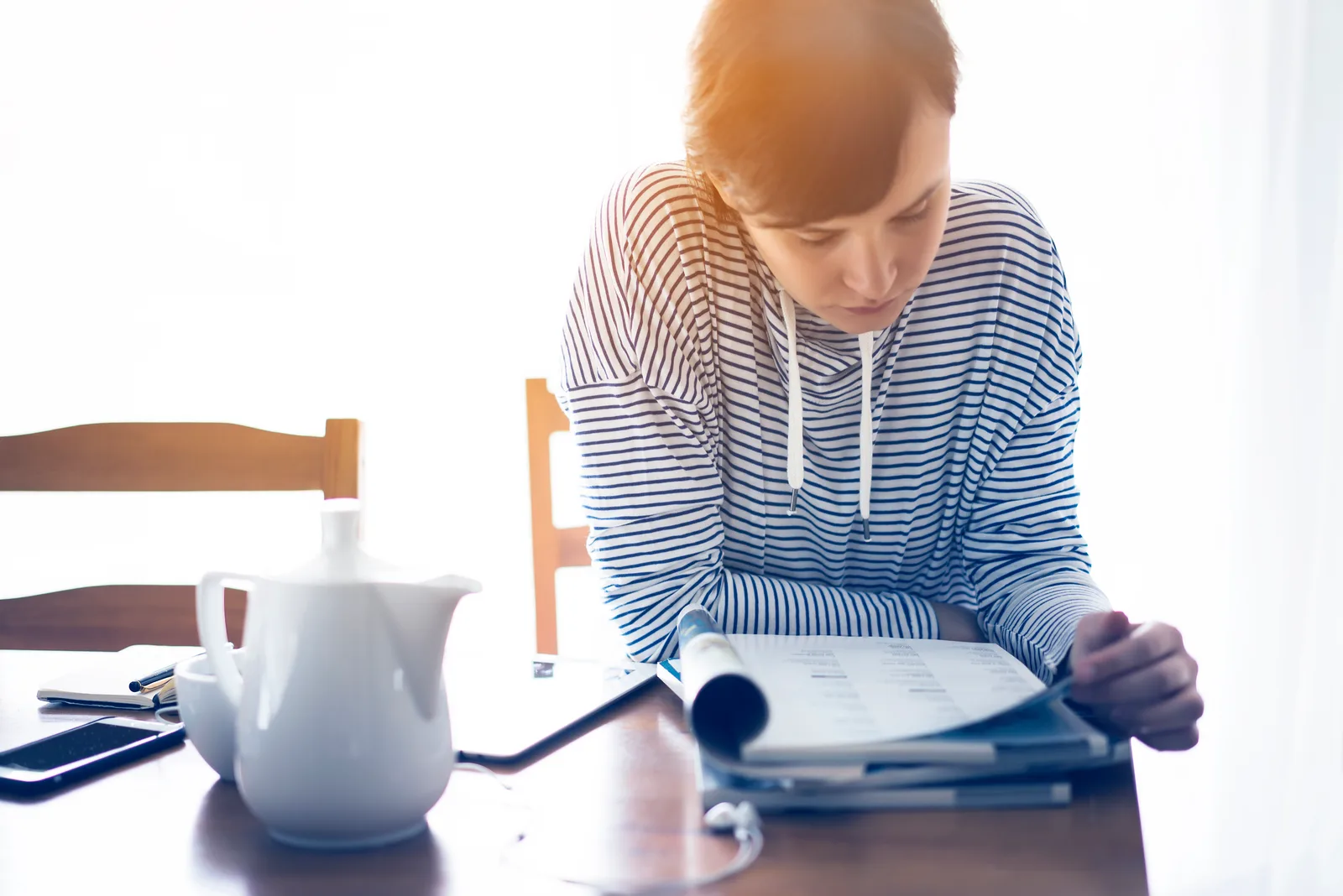 A Canadian woman reviewing tax paperwork at her kitchen table while preparing a Disability Tax Credit application.