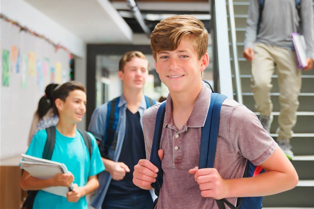 A teenage student with a backpack smiling in a busy high school hallway
